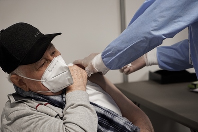Ein älterer Mann erhält die Impfung von einem Mitarbeiter des Impfzentrums in den Oberarm gespritzt.