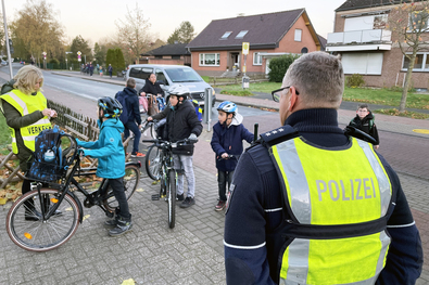 Polizei und Verkehrshelfer verteilen vor der Leegmeerschule Lose mit Gewinnzahlen an mehrere Kinder, die mit dem Fahrrad zur Schule kommen.
