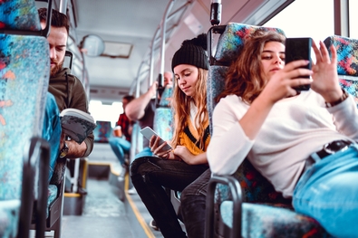 Jugendliche sitzen im Bus mit Handy und Buch.