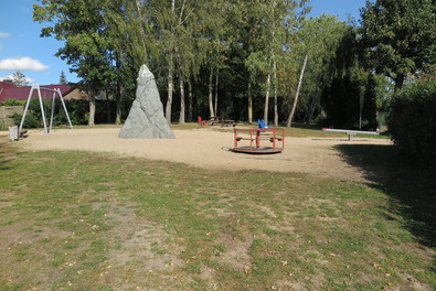 Gesamtübersicht des Spielplatz mit Kletterfelsen, Karussell und Doppelschaukel